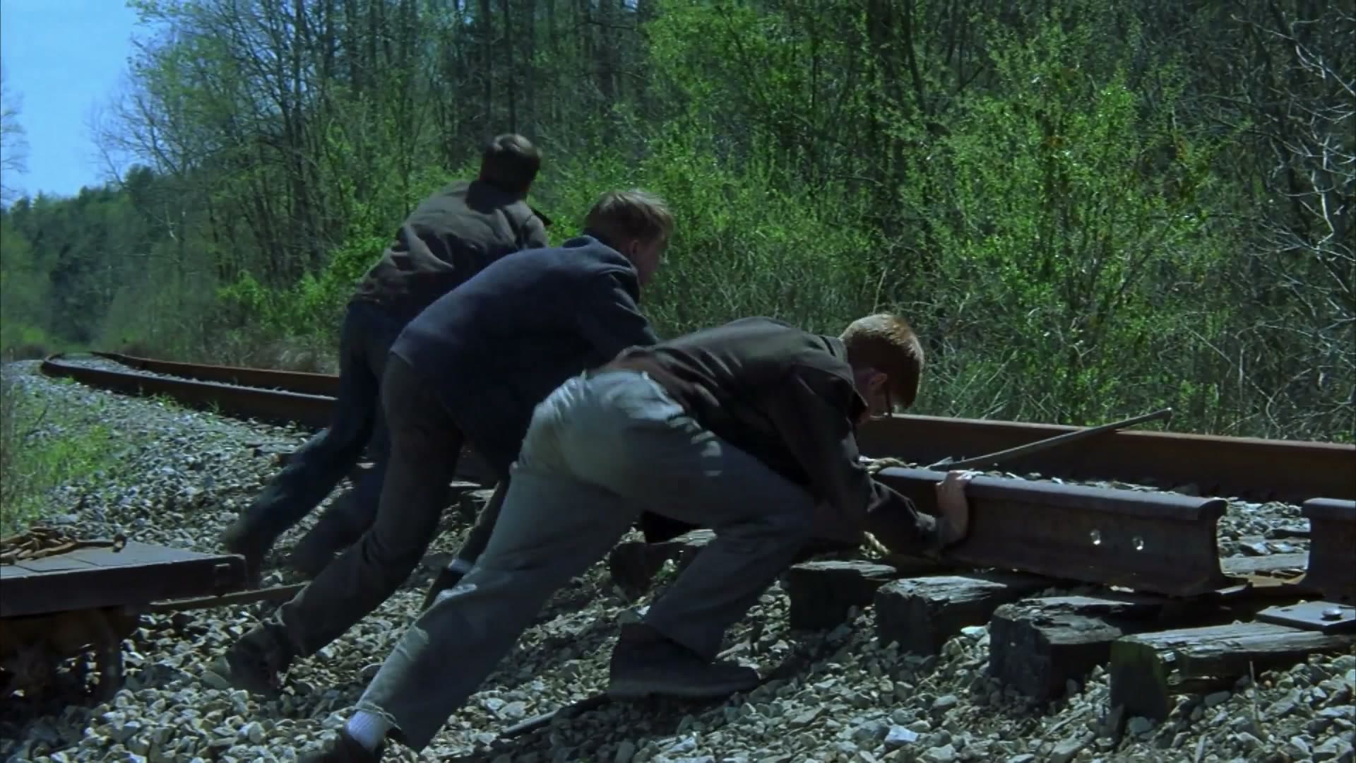 Homer e os amigos agachados sobre os trilhos de trem, em meio à mata, durante uma das aventuras do grupo