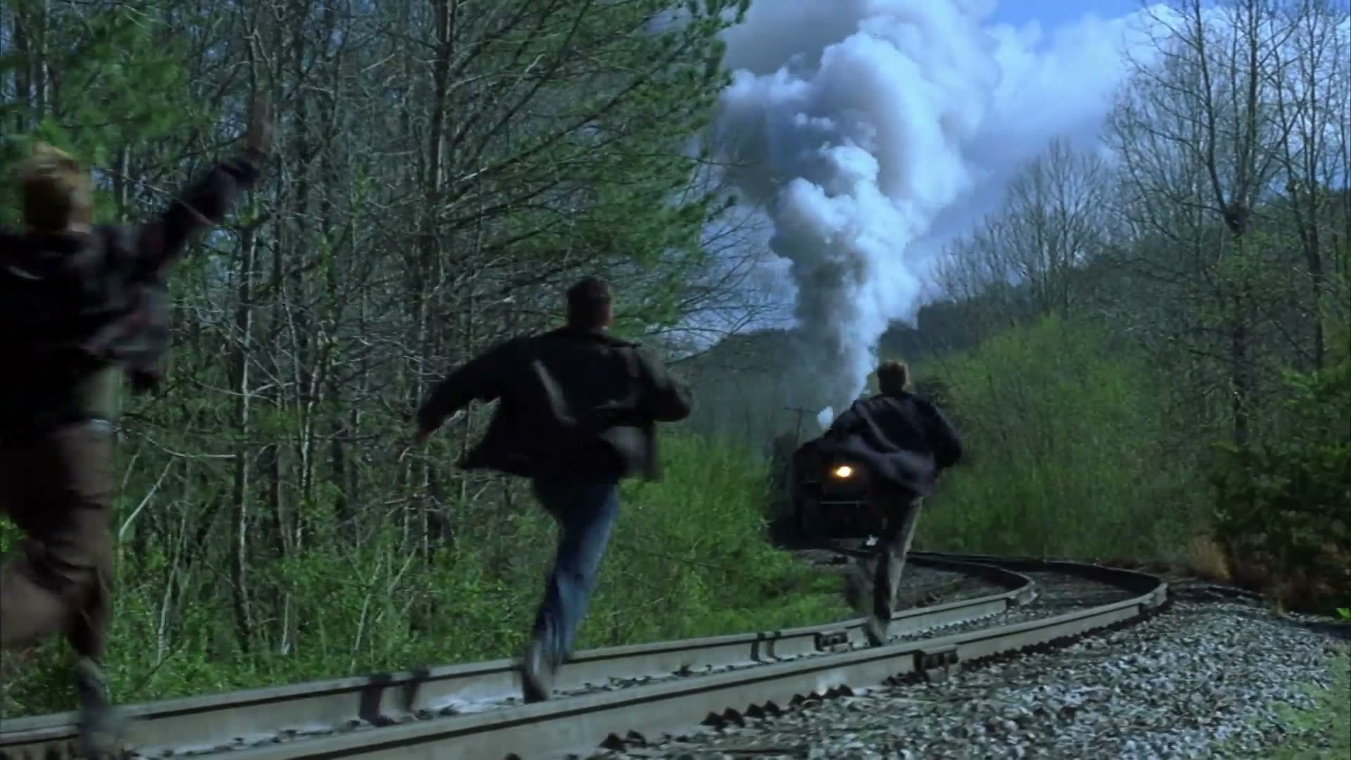 Os quatro amigos correndo pelos trilhos enquanto uma locomotiva a vapor se aproxima ao fundo